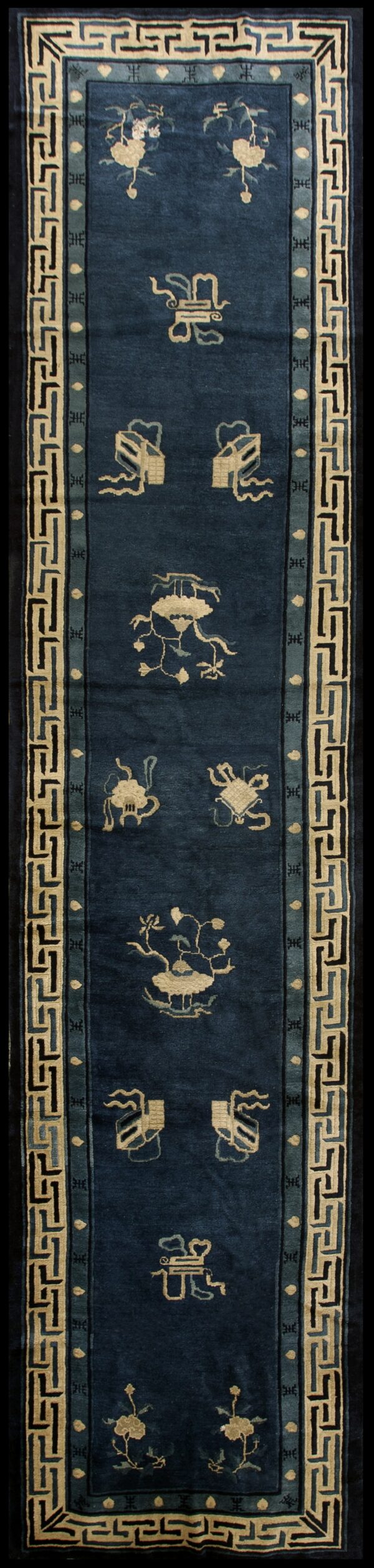 Deep blue runner rug with scattered cream motifs and a wide geometric key border in cream, black, and teal.