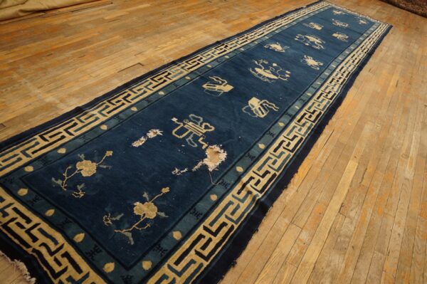 Long blue runner rug featuring tan motifs and a geometric border rests on rustic wood flooring.