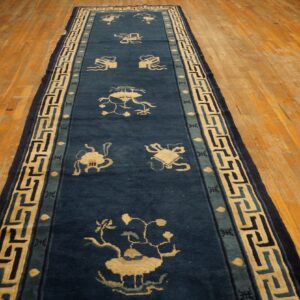 Long indigo runner with stylized beige motifs and an elaborate Greek key border on wood flooring.
