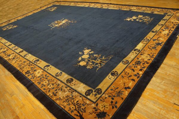 Dark blue rug features gold botanical motifs in the center field and detailed gold and navy floral borders on a wood floor.