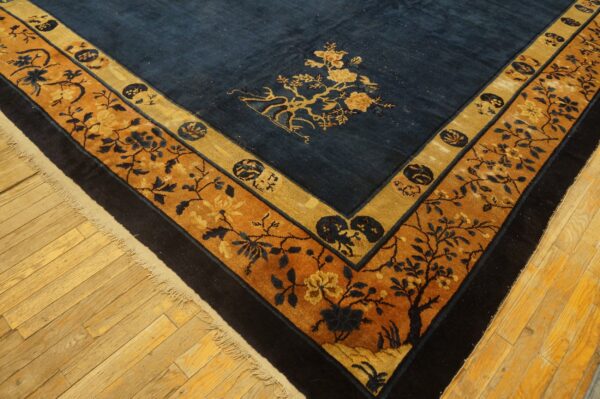 High-pile navy rug with ornate gold and rust floral borders shown on light hardwood floors.