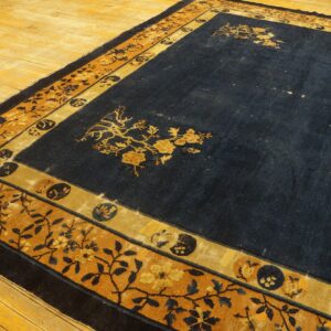 Navy blue rug with gold floral corner designs and a complex gold and dark blue patterned border on wood floorboards.