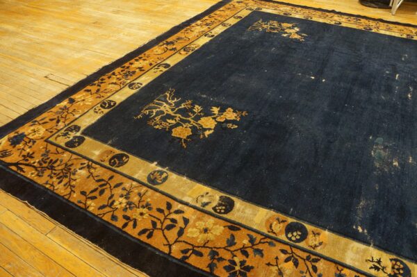 Navy blue rug with gold floral corner designs and a complex gold and dark blue patterned border on wood floorboards.