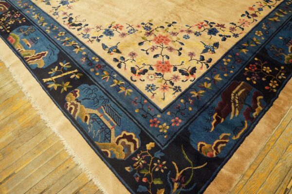 High-pile tan rug with detailed blue and navy floral and landscape borders rests on wood planks.