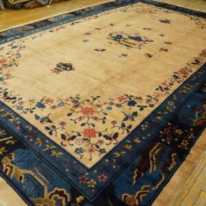Tan rug with navy and teal borders featuring floral and scenic designs rests on distressed yellow wood.