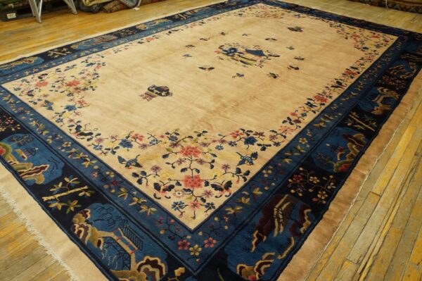 Tan rug with navy and teal borders featuring floral and scenic designs rests on distressed yellow wood.