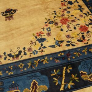 Beige field rug with colorful floral, bird, and vase motifs bordered by dark blue landscape panels.