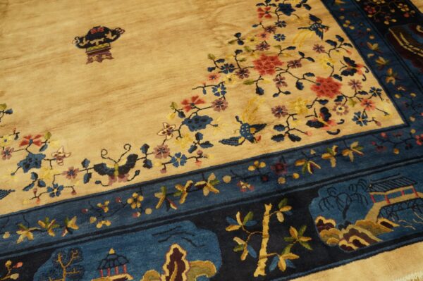 Beige field rug with colorful floral, bird, and vase motifs bordered by dark blue landscape panels.