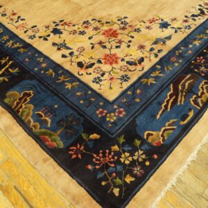 A tan rug with red florals and a complex blue border, shown on distressed yellow wooden flooring.