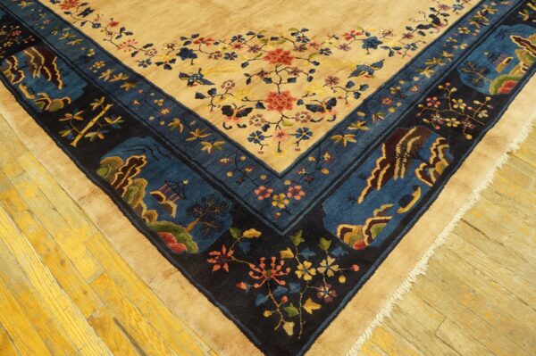A tan rug with red florals and a complex blue border, shown on distressed yellow wooden flooring.
