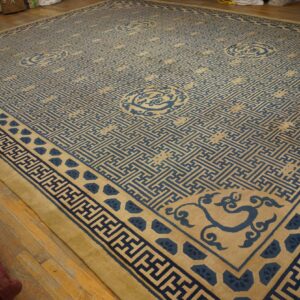 Large tan rug with blue geometric lattice and stylized corner motifs on wood floors.