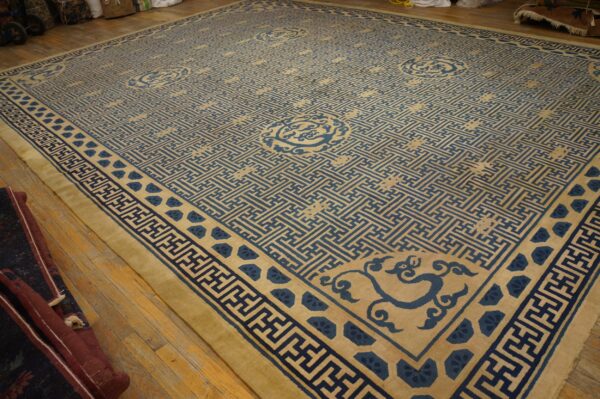 Large tan rug with blue geometric lattice and stylized corner motifs on wood floors.