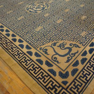 Blue geometric pattern covers the golden beige rug field and borders, set on distressed wood flooring.
