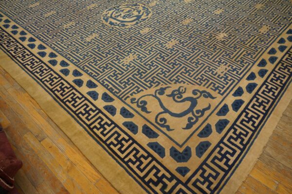 Blue geometric pattern covers the golden beige rug field and borders, set on distressed wood flooring.