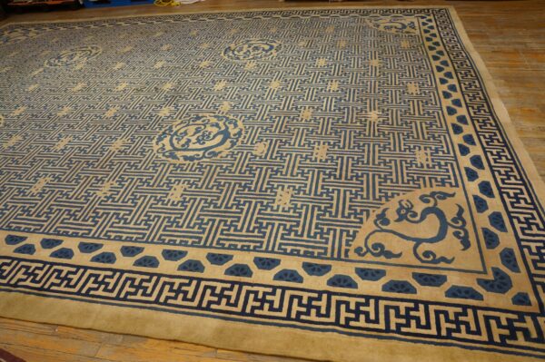 Tan rug with a dense blue interlocking maze pattern and ornamental borders rests on hardwood flooring.