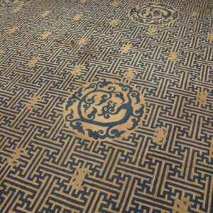 Low pile tan rug featuring a dense dark blue interlocking geometric fret pattern and ornate medallions.