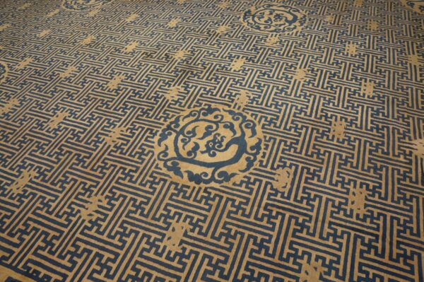 Low pile tan rug featuring a dense dark blue interlocking geometric fret pattern and ornate medallions.