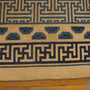 Geometric navy and tan patterned rug borders rest on light brown distressed wood flooring.