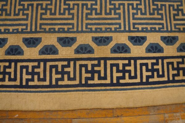 Geometric navy and tan patterned rug borders rest on light brown distressed wood flooring.