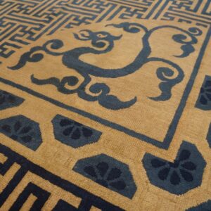 Tan rug with dark blue geometric maze, swirling cloud, and repeating floral border patterns.