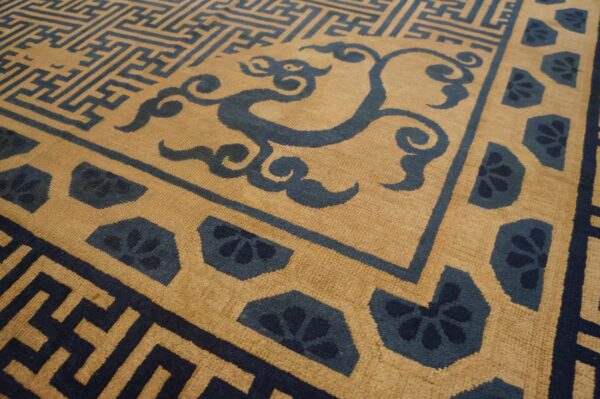 Tan rug with dark blue geometric maze, swirling cloud, and repeating floral border patterns.