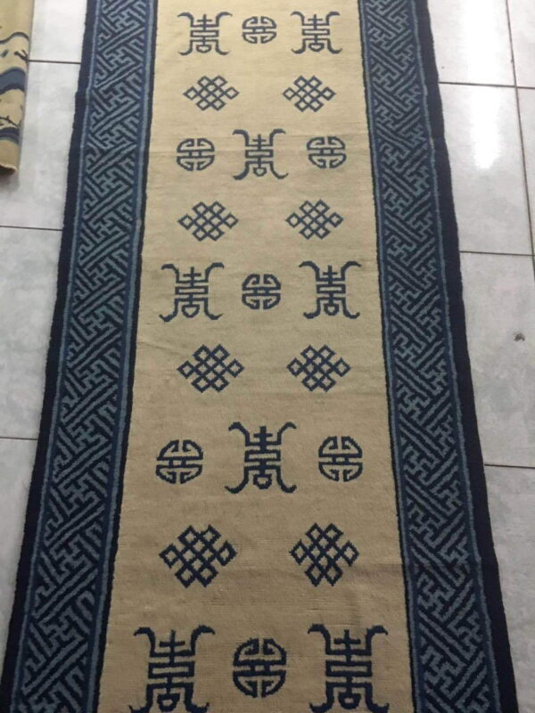 Beige runner rug with dark blue symbolic patterns and wide geometric borders on a white tile floor.