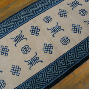 Beige runner with scattered blue auspicious symbols and a geometric fret border on wood floors.