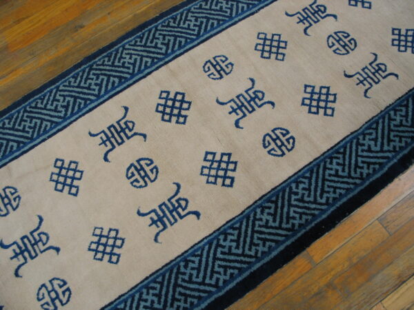 Beige runner with scattered blue auspicious symbols and a geometric fret border on wood floors.