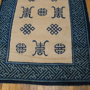 Tan rug with dark blue symbols and a wide key pattern border rests on visible hardwood flooring.