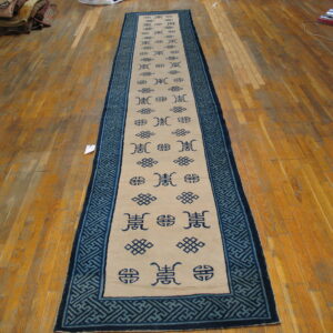 Beige runner featuring dark blue symbols and a wide geometric fretwork border rests on wood plank flooring.