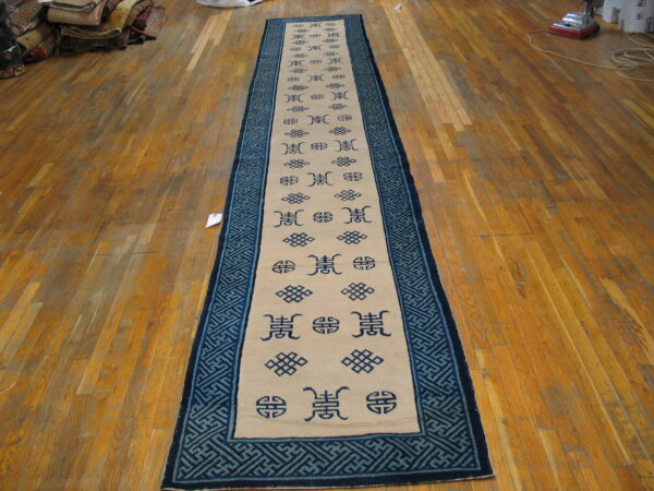 Beige runner featuring dark blue symbols and a wide geometric fretwork border rests on wood plank flooring.