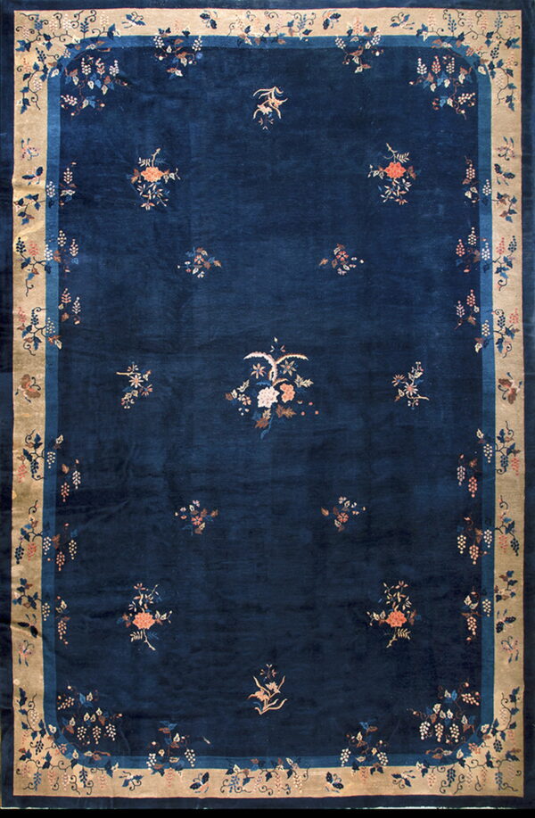 Deep navy rug with a wide beige border and stylized floral and grapevine patterns in pinks and blues.
