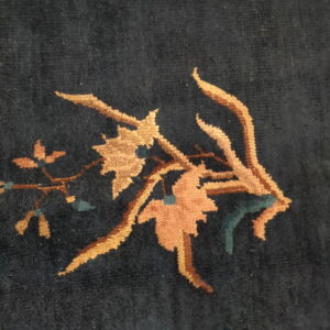 Dark navy rug close-up showing a medium pile and a botanical design in gold, rust, and teal.