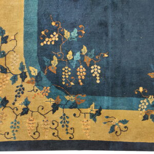 Corner view of a high-pile rug showing a navy field, gold border, and stylized grape and vine pattern.