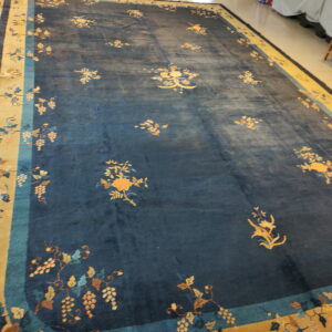 Navy blue area rug with scattered orange floral designs and a border depicting grape clusters on tile flooring.