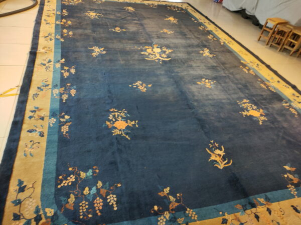 Navy blue area rug with scattered orange floral designs and a border depicting grape clusters on tile flooring.