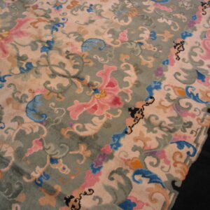 High-pile rug featuring scrolling floral patterns in pink, blue, orange, and green on a pale beige field.