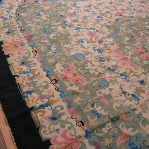 Ornate floral rug featuring pink, blue, and sage colors on a cream field with a black curved border.
