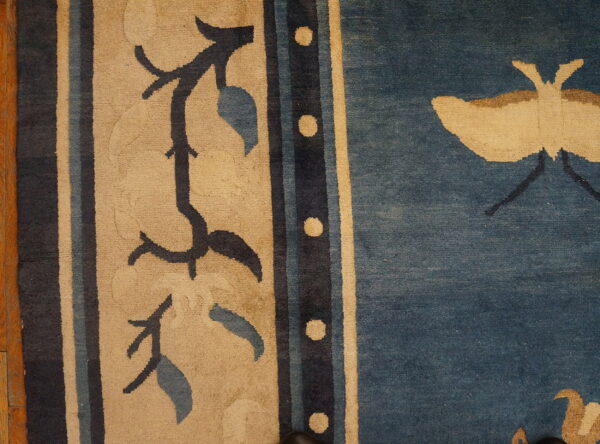 Beige border with dark floral vines next to a blue field featuring a large beige butterfly.