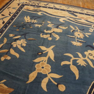 Blue rug with large cream and tan traditional floral and vine motifs on hardwood floors.