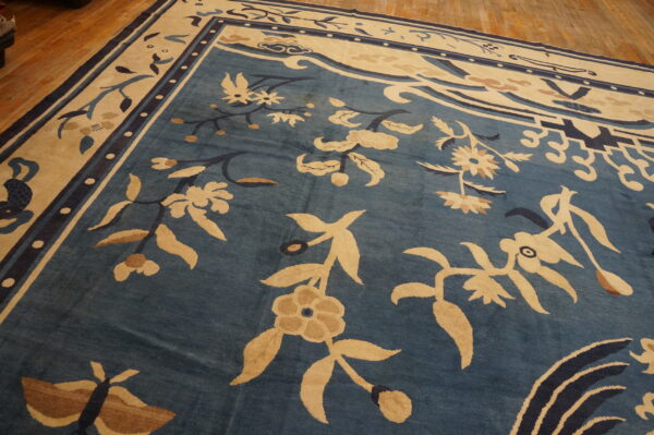 Blue rug with large cream and tan traditional floral and vine motifs on hardwood floors.