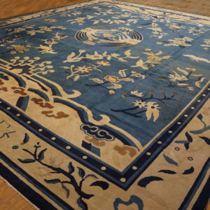 Blue rug with extensive beige and navy floral patterns, a central medallion, and wide border rests on wood flooring.