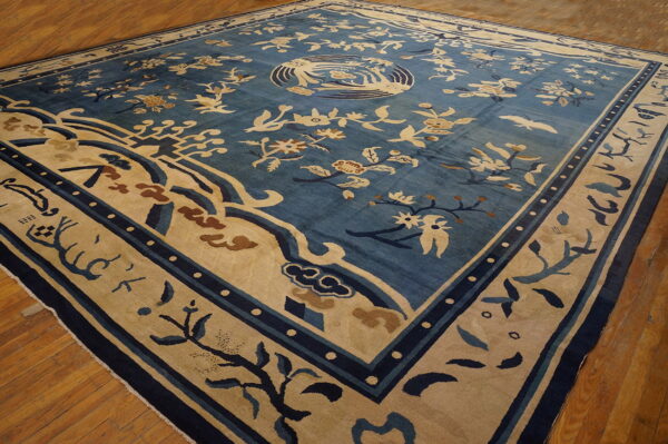 Blue rug with extensive beige and navy floral patterns, a central medallion, and wide border rests on wood flooring.