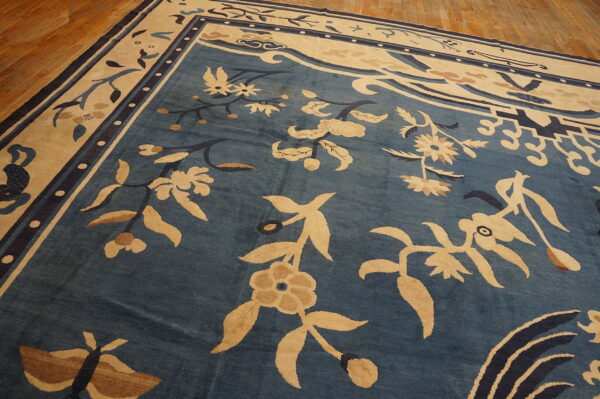 Ornate blue and tan traditional rug with large floral patterns and distressed texture on wood planks.
