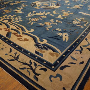 Blue high-pile rug with tan, rust, and navy floral patterns rests on a wooden floor.