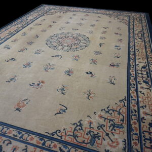 Beige low pile rug featuring scattered blue and coral floral motifs and intricate multi-layered borders.