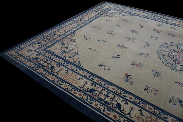 Tan rug with scattered blue and pink floral motifs and complex borders featuring navy and rust designs.
