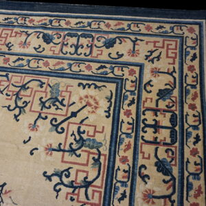 Corner view of a rug featuring a cream field surrounded by dark blue and red patterned borders.