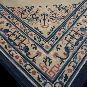 Detailed view of a rug corner with beige field, dark blue borders, and stylized red and blue floral patterns.