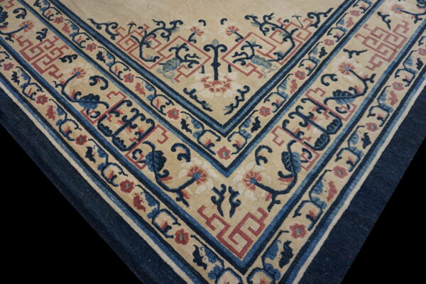 Detailed view of a rug corner with beige field, dark blue borders, and stylized red and blue floral patterns.